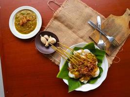 Sate Padang or satay padang is Spicy beef satay from Padang, West Sumatra. Served with spicy curry sauce and rice cake, lontong on banana leaf. isolated on white background photo