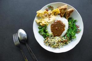 Nasi Pecel or sego pecel is Traditional Javanese rice dish of steamed rice with vegetable salad, peanut sauce, tempeh, tofu bean sprouts and crackers or peyek kacang. on black backgroud photo