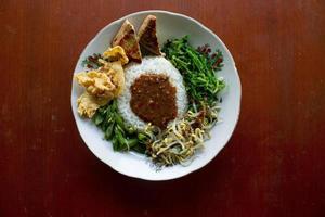 Nasi Pecel or sego pecel is Traditional Javanese rice dish of steamed rice with vegetable salad, peanut sauce, tempeh, tofu bean sprouts and crackers or peyek kacang. on black backgroud photo