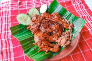 grilled chicken or ayam bakar with cucumber slash served on banana leaf and plate. ayam bakar is traditional grilled chicken from indonesia photo