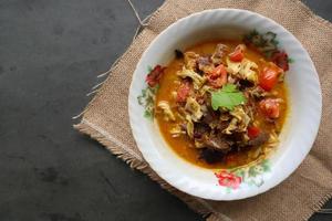 Goat Curry or gulai kambing, food from asia. Delicious goat meat curry served in a bowl.served with tomato, seasoning, celery and cabbage photo
