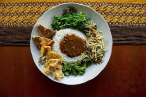 Nasi Pecel or sego pecel is Traditional Javanese rice dish of steamed rice with vegetable salad, peanut sauce, tempeh, tofu bean sprouts and crackers or peyek kacang. on black backgroud photo