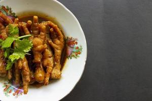 patas de pollo picantes con apio, chile, cebolla, ajo servido con un plato blanco aislado de un fondo negro. foto