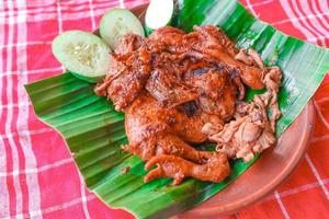 grilled chicken or ayam bakar with cucumber slash served on banana leaf and plate. ayam bakar is traditional grilled chicken from indonesia photo