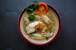 Chicken soup served with vegetables, tomatoes, celery in a bowl, spoon and fork. with black background photo