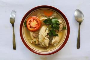 Chicken soup served with vegetables, tomatoes, celery in a bowl, spoon and fork. with black background photo