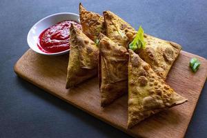 Samosa, samsa or somsa are triangular fried pastries or pastri served with tomato sauce and leek slice, on black background photo