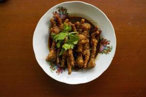 Spicy chicken feet with celery, chili, onion, garlic served with a white plate isolated from a black background. photo