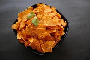 el chip de tortilla es chips de maíz o nachos llamados, servidos en un tazón, sobre fondo negro hecho de maíz foto