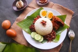 nasi lemak, es un malayo tradicional hecho con huevos cocidos, frijoles, anchoas, salsa de chile, pepino. del plato servido en una hoja de plátano foto