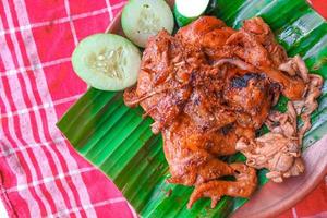 grilled chicken or ayam bakar with cucumber slash served on banana leaf and plate. ayam bakar is traditional grilled chicken from indonesia photo