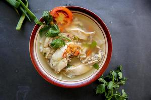 Chicken soup served with vegetables, tomatoes, celery in a bowl, spoon and fork. with black background photo