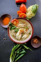 Chicken soup served with vegetables, tomatoes, celery in a bowl, spoon and fork. with black background photo