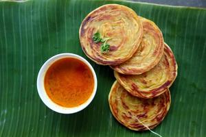 pan paratha o pan canai o roti maryam, plato de desayuno favorito. servido en licencia de plátano foto