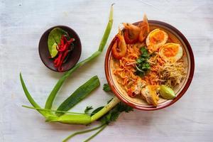 laksa, laksa curry made from vermicelli, noodles, bean sprouts, egg, tofu lime, and shrimp with a spicy soup sauce that is rich in spices. laksa served on bowl, isolated on white background. photo