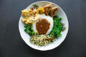 Nasi Pecel or sego pecel is Traditional Javanese rice dish of steamed rice with vegetable salad, peanut sauce, tempeh, tofu bean sprouts and crackers or peyek kacang. on black backgroud photo