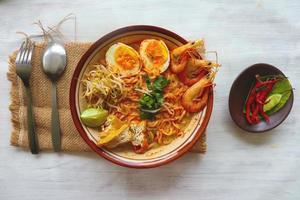 laksa, laksa curry made from vermicelli, noodles, bean sprouts, egg, tofu lime, and shrimp with a spicy soup sauce that is rich in spices. laksa served on bowl, isolated on white background. photo
