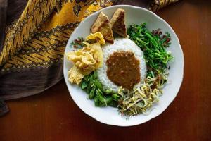 Nasi Pecel or sego pecel is Traditional Javanese rice dish of steamed rice with vegetable salad, peanut sauce, tempeh, tofu bean sprouts and crackers or peyek kacang. on black backgroud photo