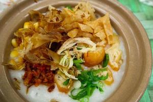 porridge served on hot claypot topped with chicken, sweet corn, skipjack tuna, tofu, green onions, crackers, dumplings and broth photo