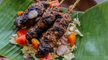 sate buntel o satay buntel es satay hecho de cordero picado envuelto en grasa de cordero y luego asado a la parrilla. condimento con tomates, chalotes, pimienta, repollo foto