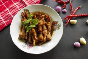 Spicy chicken feet with celery, chili, onion, garlic served with a white plate isolated from a black background. photo