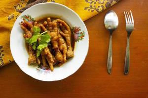 Spicy chicken feet with celery, chili, onion, garlic served with a white plate isolated from a black background. photo