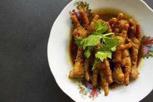 Spicy chicken feet with celery, chili, onion, garlic served with a white plate isolated from a black background. photo