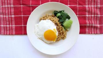 fideos instantáneos servidos con huevo frito y hojas de mostaza en un plato. indomie de fideos fritos instantáneos foto