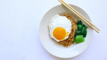 fideos instantáneos servidos con huevo frito y hojas de mostaza en un plato. indomie de fideos fritos instantáneos foto