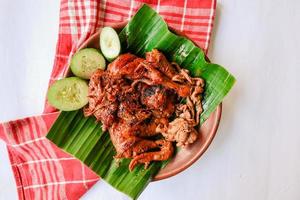 pollo a la parrilla o ayam bakar con pepino servido en hoja de plátano y plato. ayam bakar es pollo asado tradicional de indonesia foto