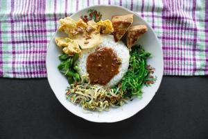 Nasi Pecel or sego pecel is Traditional Javanese rice dish of steamed rice with vegetable salad, peanut sauce, tempeh, tofu bean sprouts and crackers or peyek kacang. on black backgroud photo