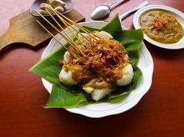 Sate Padang or satay padang is Spicy beef satay from Padang, West Sumatra. Served with spicy curry sauce and rice cake, lontong on banana leaf. isolated on white background photo