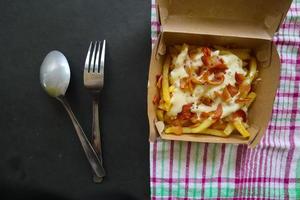 fried fries with with melted cheddar cheese or fried cheese with topping sausage slices on box photo