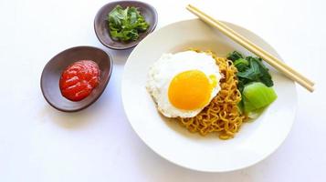 fideos instantáneos servidos con huevo frito y hojas de mostaza en un plato. indomie de fideos fritos instantáneos foto