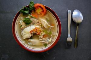 Chicken soup served with vegetables, tomatoes, celery in a bowl, spoon and fork. with black background photo