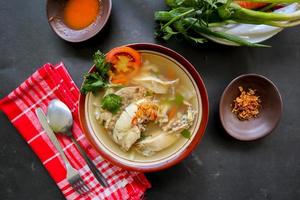Chicken soup served with vegetables, tomatoes, celery in a bowl, spoon and fork. with black background photo
