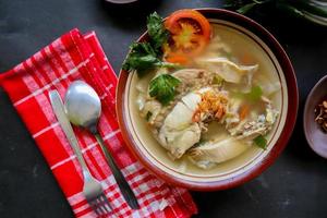 Chicken soup served with vegetables, tomatoes, celery in a bowl, spoon and fork. with black background photo