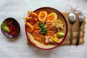 laksa, laksa curry made from vermicelli, noodles, bean sprouts, egg, tofu lime, and shrimp with a spicy soup sauce that is rich in spices. laksa served on bowl, isolated on white background. photo