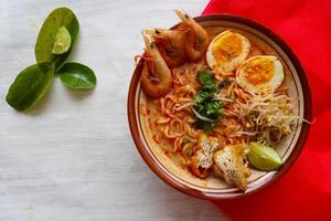 laksa, laksa curry made from vermicelli, noodles, bean sprouts, egg, tofu lime, and shrimp with a spicy soup sauce that is rich in spices. laksa served on bowl, isolated on white background. photo