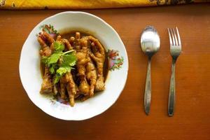 Spicy chicken feet with celery, chili, onion, garlic served with a white plate isolated from a black background. photo