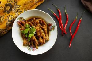 Spicy chicken feet with celery, chili, onion, garlic served with a white plate isolated from a black background. photo