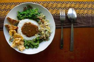 Nasi Pecel or sego pecel is Traditional Javanese rice dish of steamed rice with vegetable salad, peanut sauce, tempeh, tofu bean sprouts and crackers or peyek kacang. on black backgroud photo