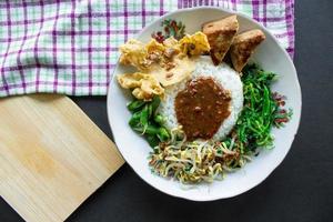 Nasi Pecel or sego pecel is Traditional Javanese rice dish of steamed rice with vegetable salad, peanut sauce, tempeh, tofu bean sprouts and crackers or peyek kacang. on black backgroud photo