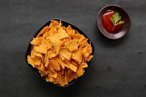 el chip de tortilla es chips de maíz o nachos llamados, servidos en un tazón, sobre fondo negro hecho de maíz foto