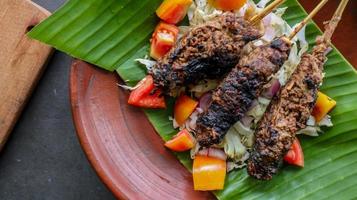 sate buntel o satay buntel es satay hecho de cordero picado envuelto en grasa de cordero y luego asado a la parrilla. condimento con tomates, chalotes, pimienta, repollo foto