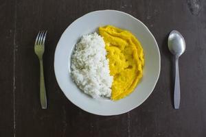 a photo rice with fried egg omelet, with spoon and fork on white plate. isolated on wood background. breakfast with omelet in morning