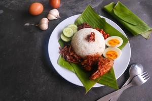 nasi lemak, es un malayo tradicional hecho con huevos cocidos, frijoles, anchoas, salsa de chile, pepino. del plato servido en una hoja de plátano foto