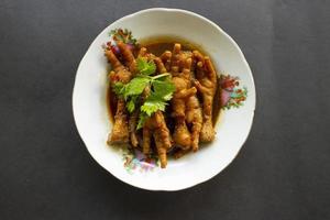 Spicy chicken feet with celery, chili, onion, garlic served with a white plate isolated from a black background. photo