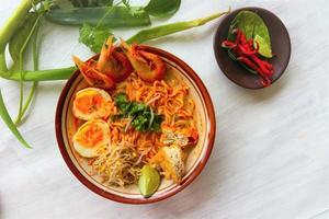 laksa, laksa curry made from vermicelli, noodles, bean sprouts, egg, tofu lime, and shrimp with a spicy soup sauce that is rich in spices. laksa served on bowl, isolated on white background. photo