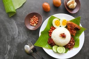 nasi lemak, es un malayo tradicional hecho con huevos cocidos, frijoles, anchoas, salsa de chile, pepino. del plato servido en una hoja de plátano foto